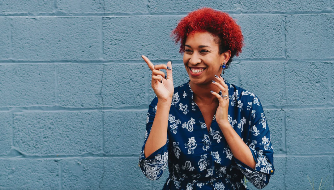 person with red hair smiling and pointing in front of blue gray wall