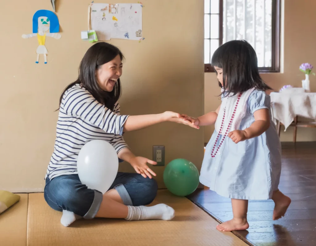 Mother playing with toddler girl and balloons indoors