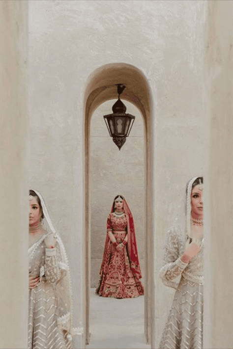 Unique editorial wedding photograph of a bride in red framed by bridesmaids in grey, posed artistically through archways, highlighting high-fashion and symmetry in wedding photography.