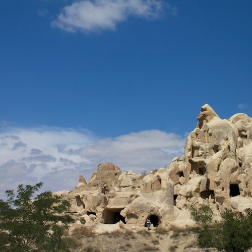 Rock formations with natural caves under a blue sky with some clouds and sparse greenery in the foreground.