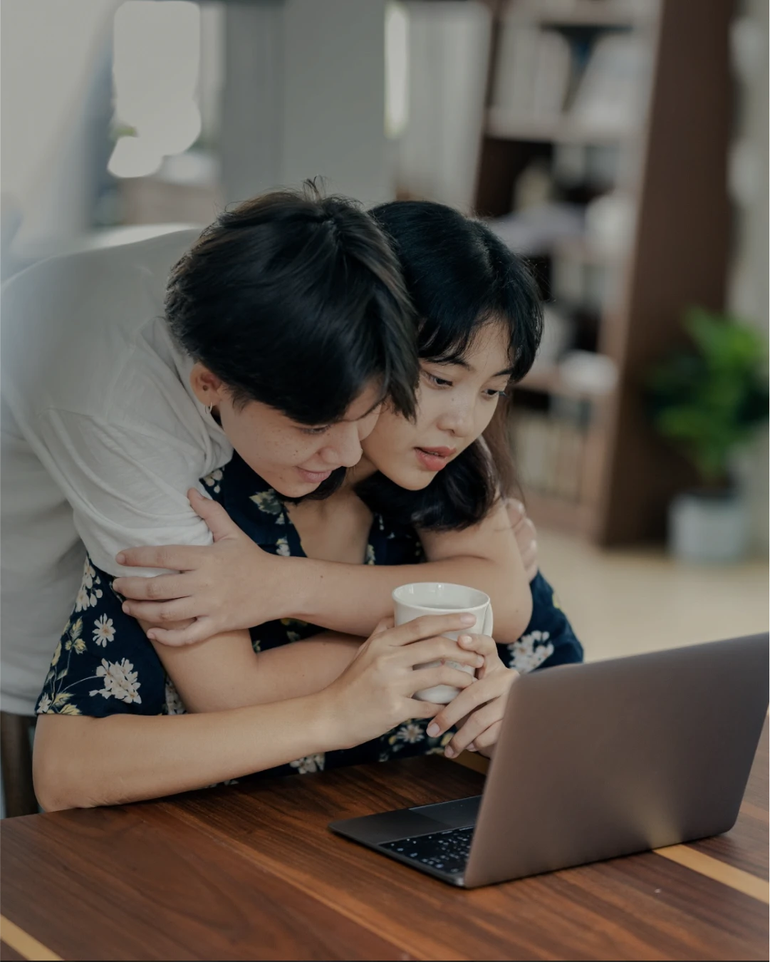 A man wraps his arms around his boyfriend, looking at the computer screen together