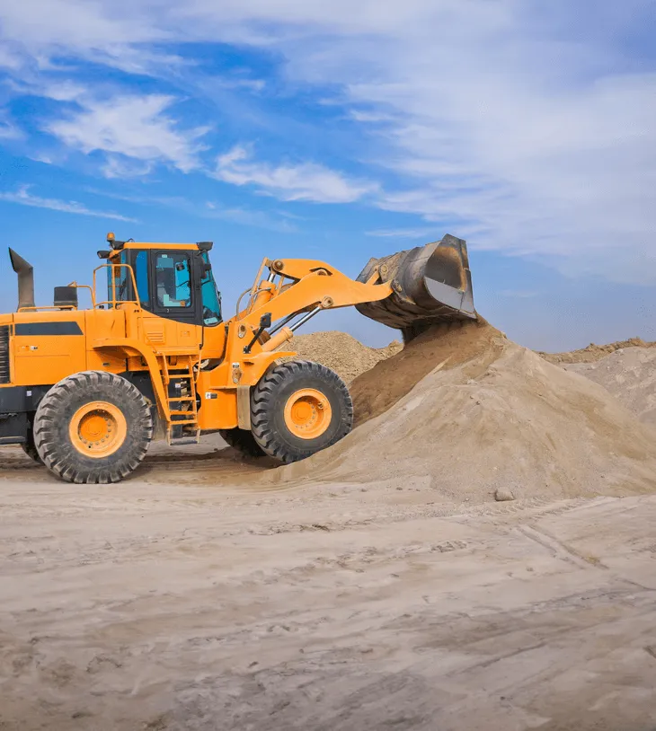 A front loader tipping sand onto a pile of more sand in a quarry