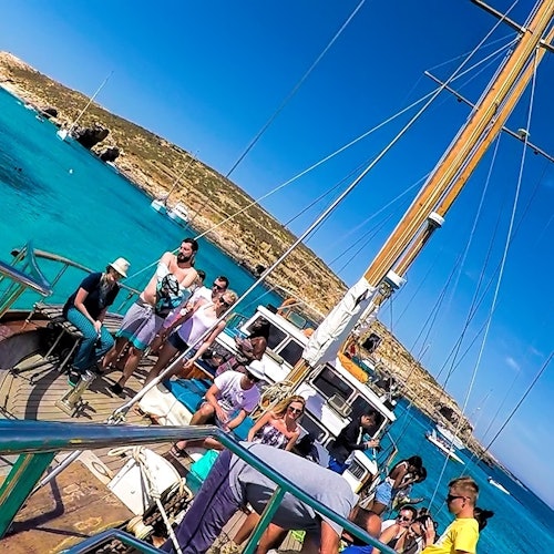 People enjoying a sunny day on a boat with turquoise water and rocky shores in the background.