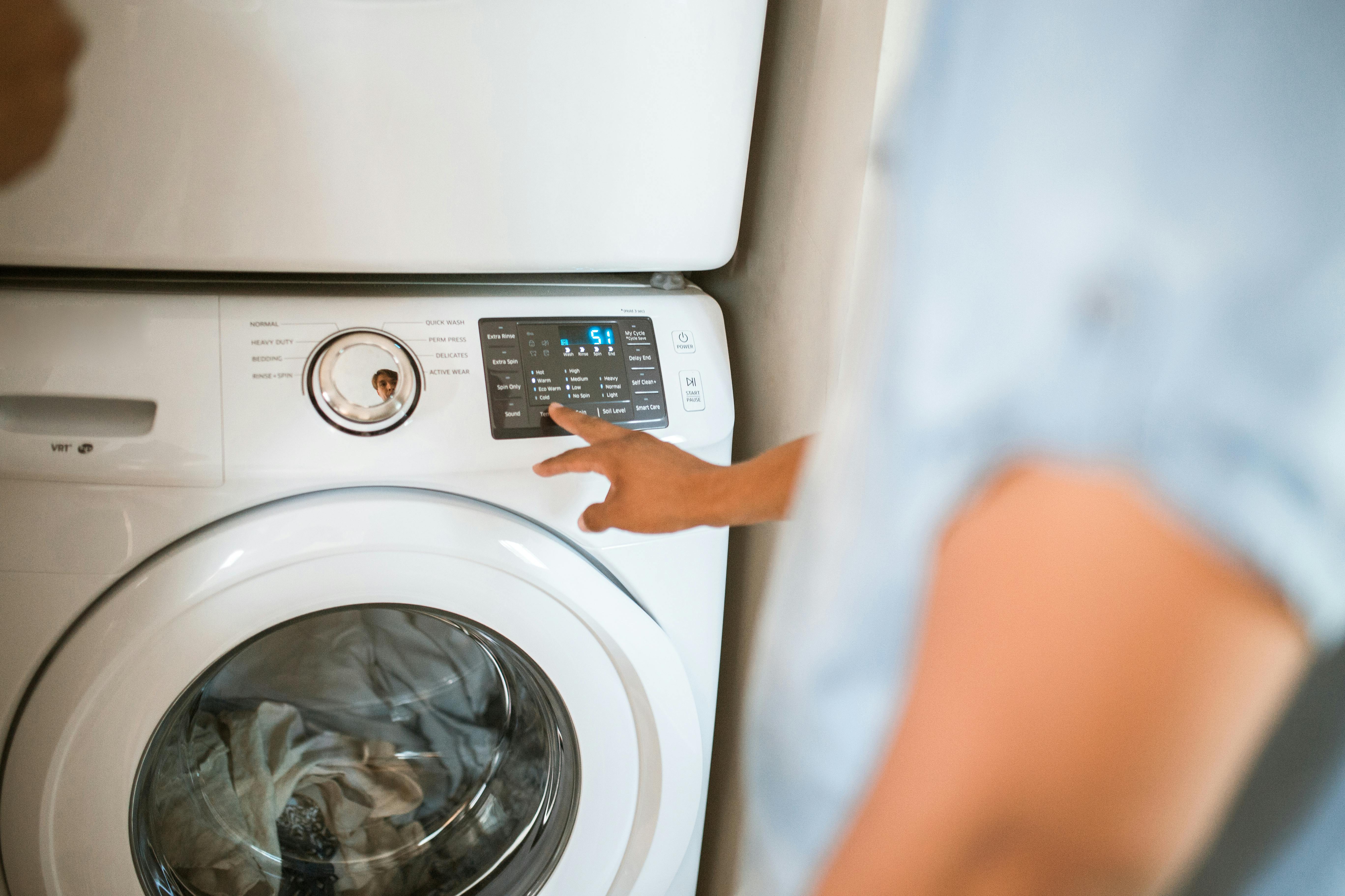 Person selecting cycle settings on modern stacked washer and dryer, illustrating features to compare when choosing the best washer/dryer manufacturers.