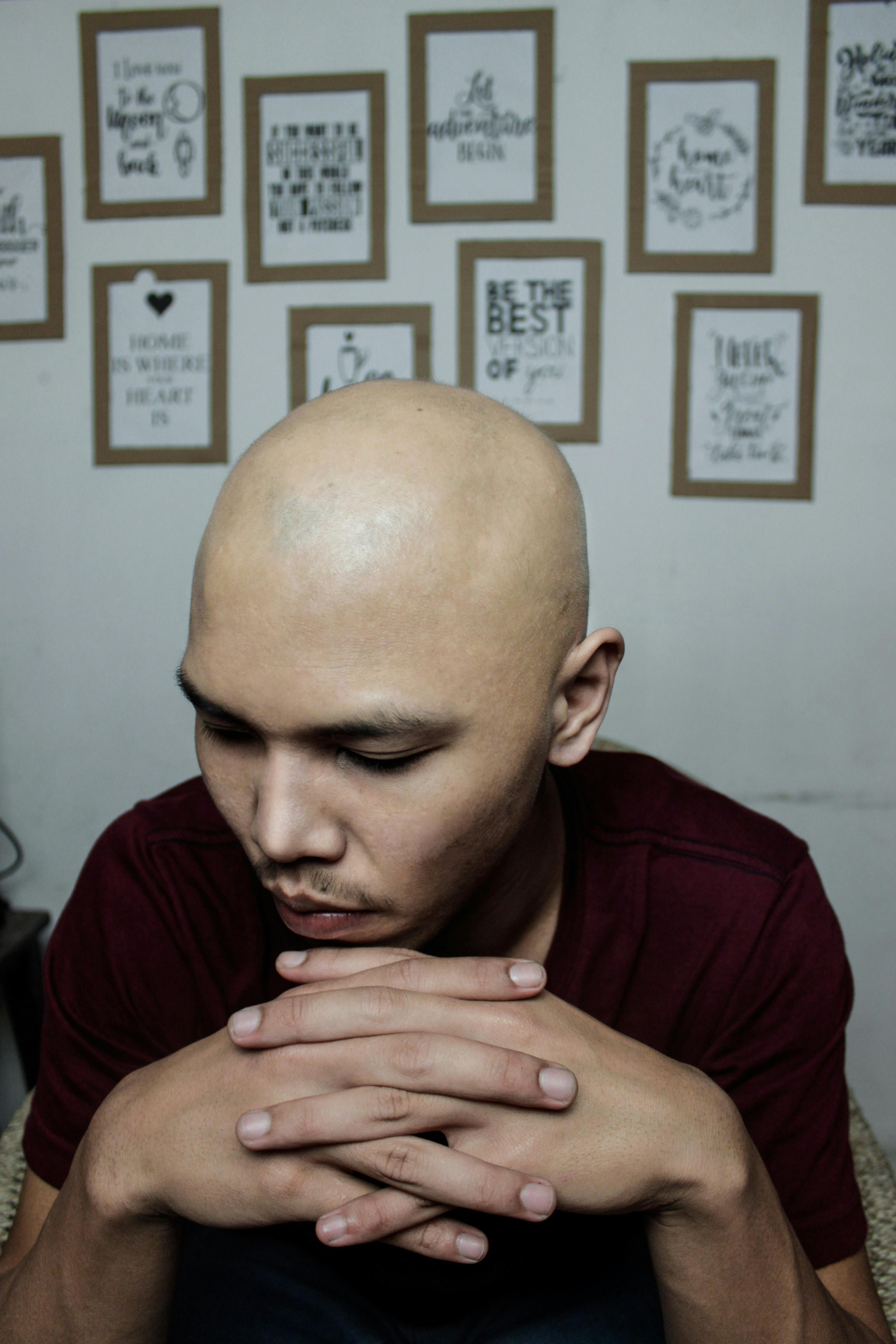 bald-man-sitting-indoors,-hands-together,-with-motivational-quotes-on-the-wall. - eminumana (pexels)