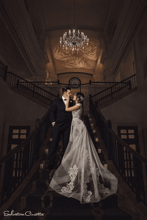 Glamorous and moody wedding portrait of a couple embracing on an opulent staircase, with dramatic lighting enhancing the atmosphere in this style of photography.