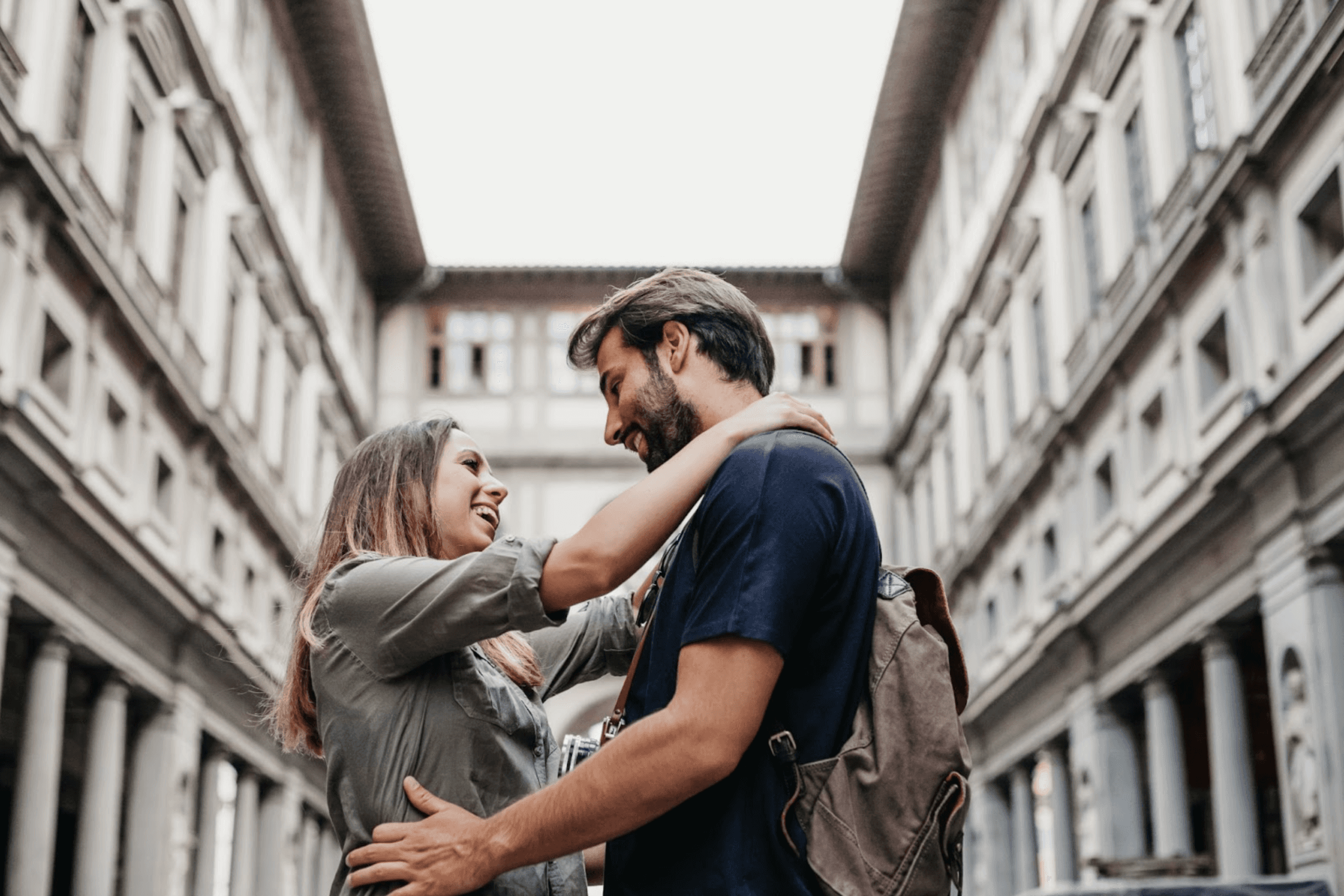 Koppel glimlachend en omarmend in een smalle Europese straat met historische gebouwen.