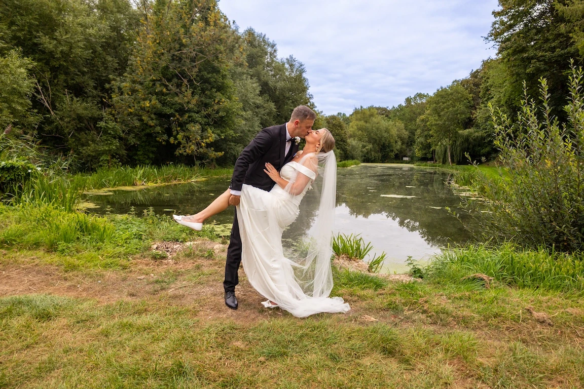 Charlotte and Chris sharing a kiss by the lake at The Great Barn Aynho