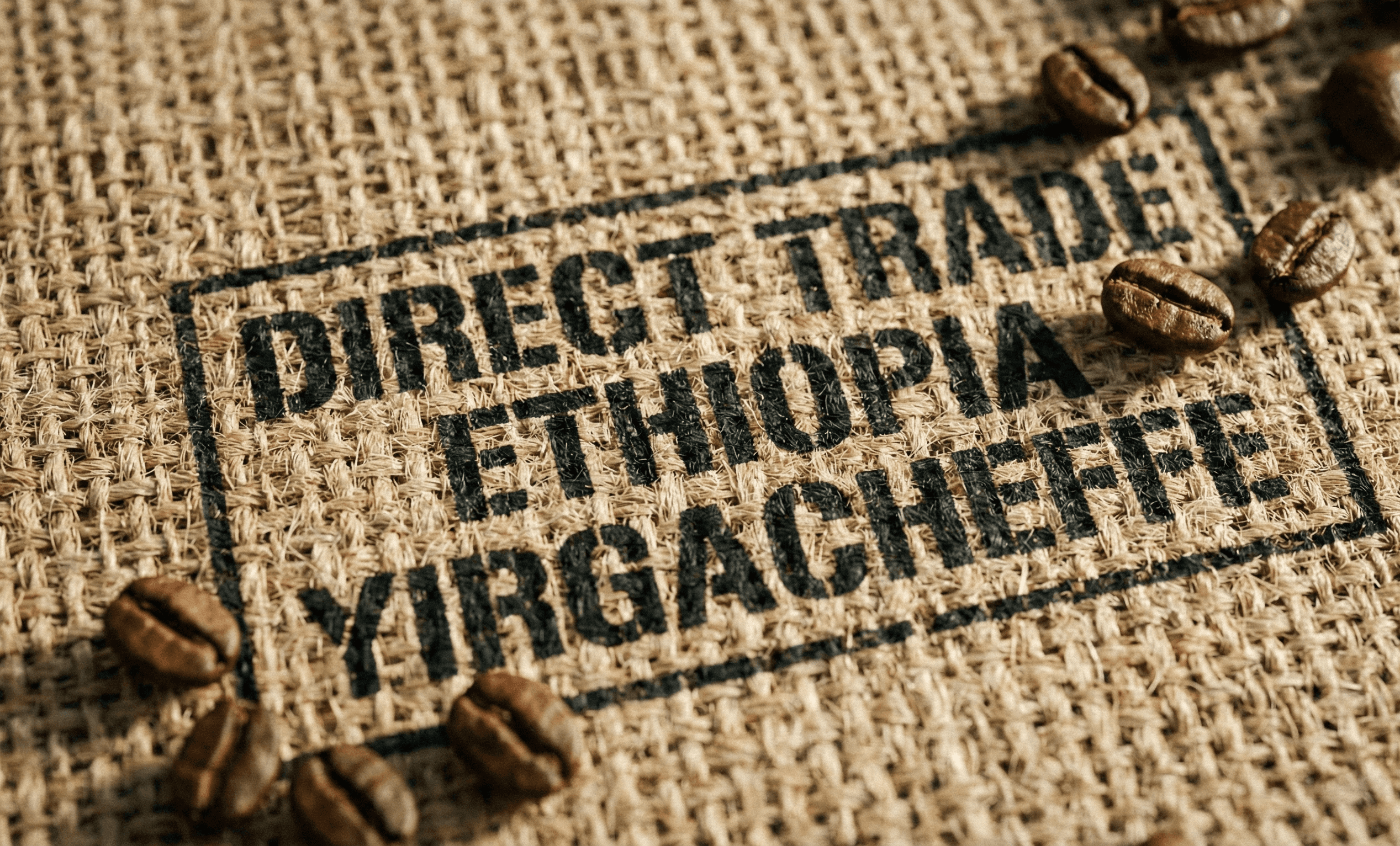 Texture detail of a burlap coffee sack stamped with origin information and scattered roasted coffee beans