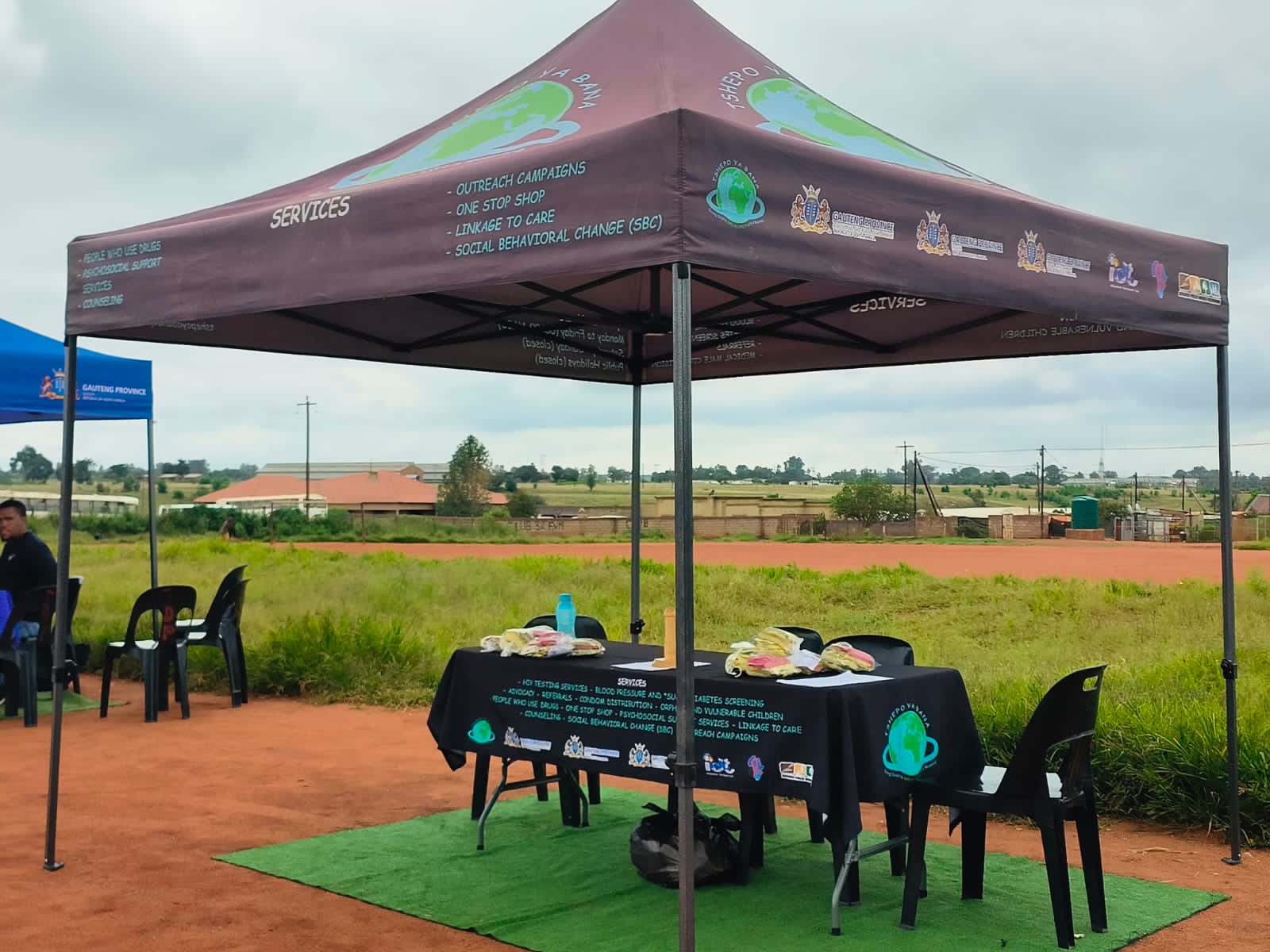 A smiling young man with crossed arms, wearing a plaid shirt and white t-shirt, poses against a dark background.