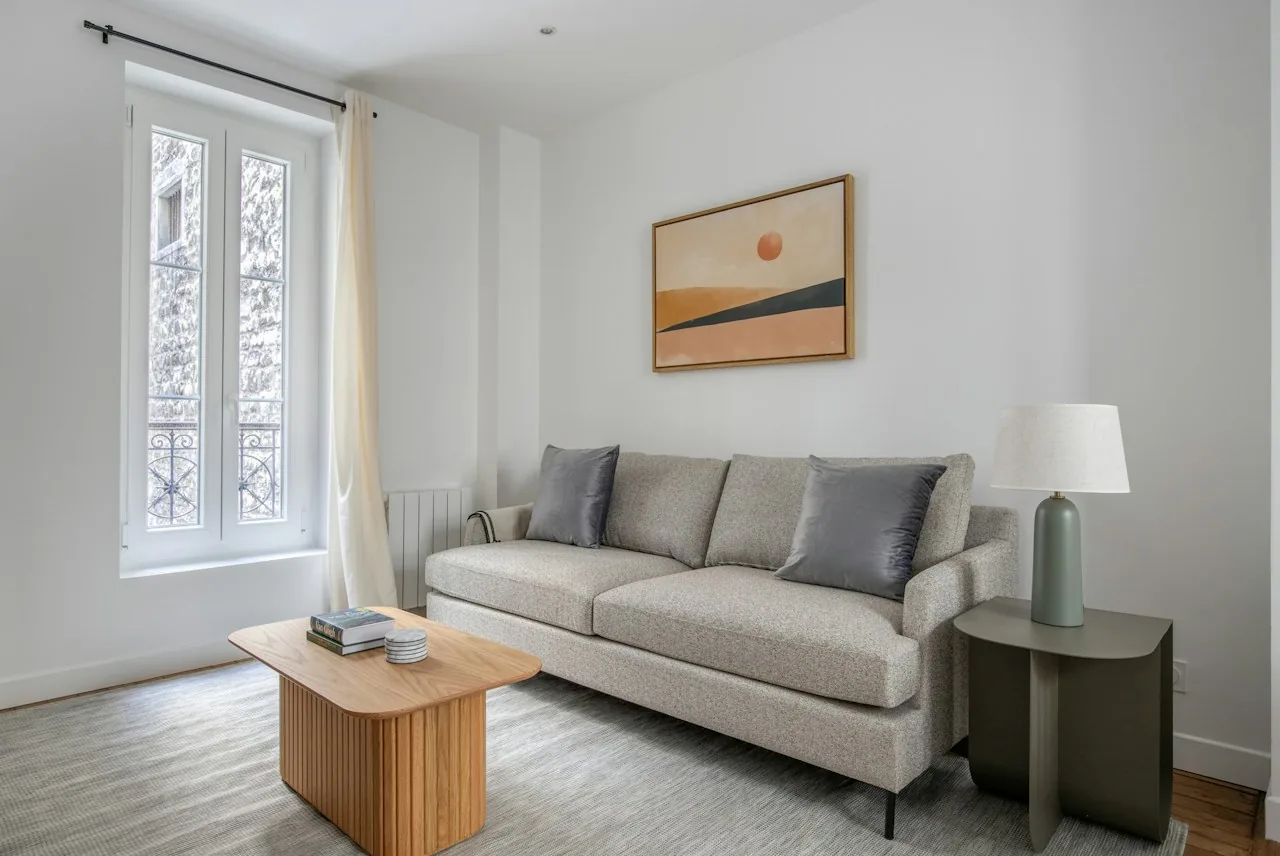 Salon d’un appartement meublé avec canapé gris et fenêtre à la française