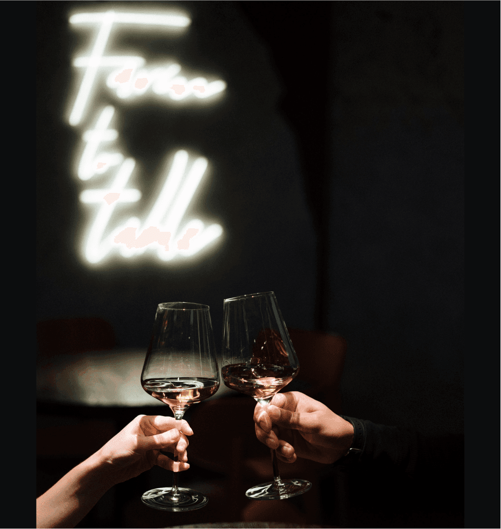 People clinking glasses, with a neon sign in the background.