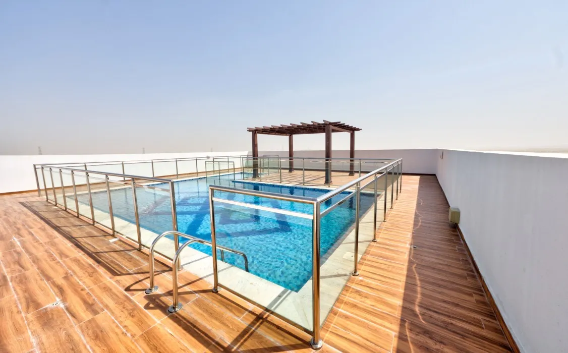 A pool with a glass railing and deck at Al Haseen Residence, showcasing a modern outdoor living space.