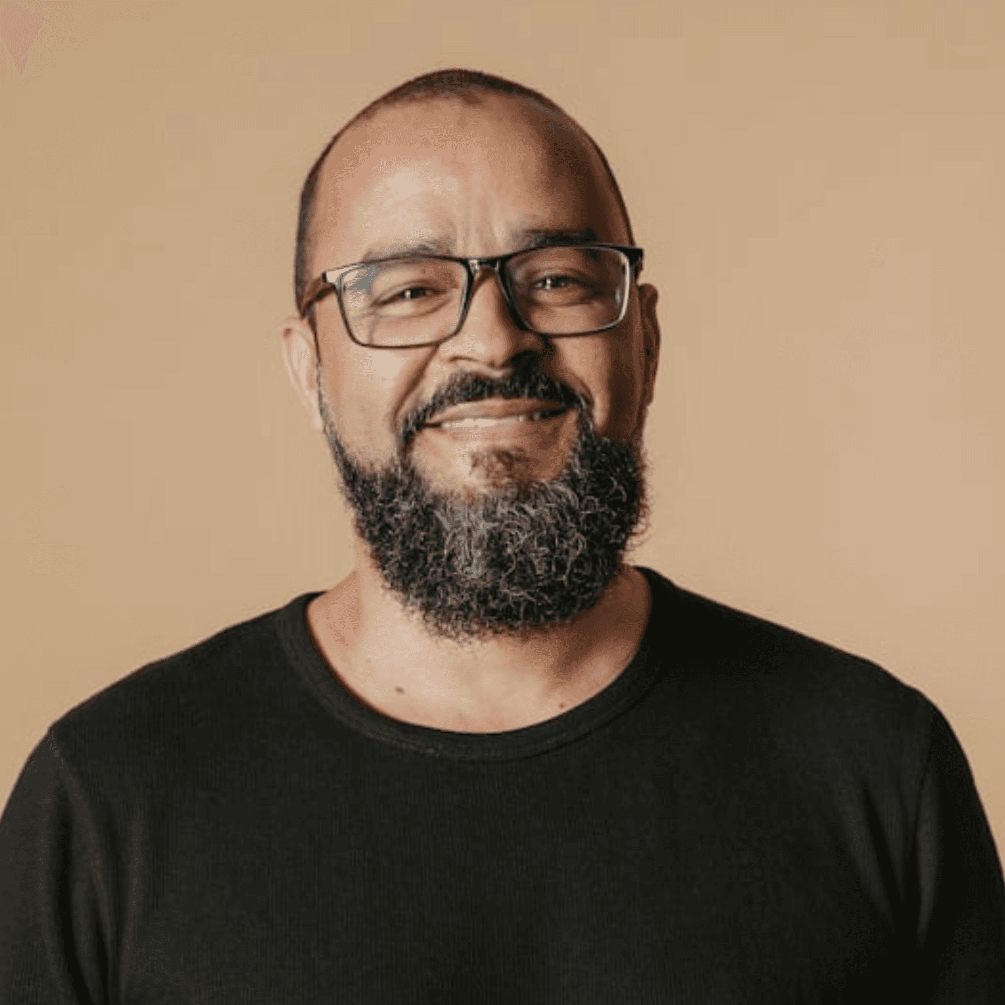 Smiling man with glasses and a short beard wearing a white t-shirt stands against a deep purple background, conveying a cheerful and friendly tone.