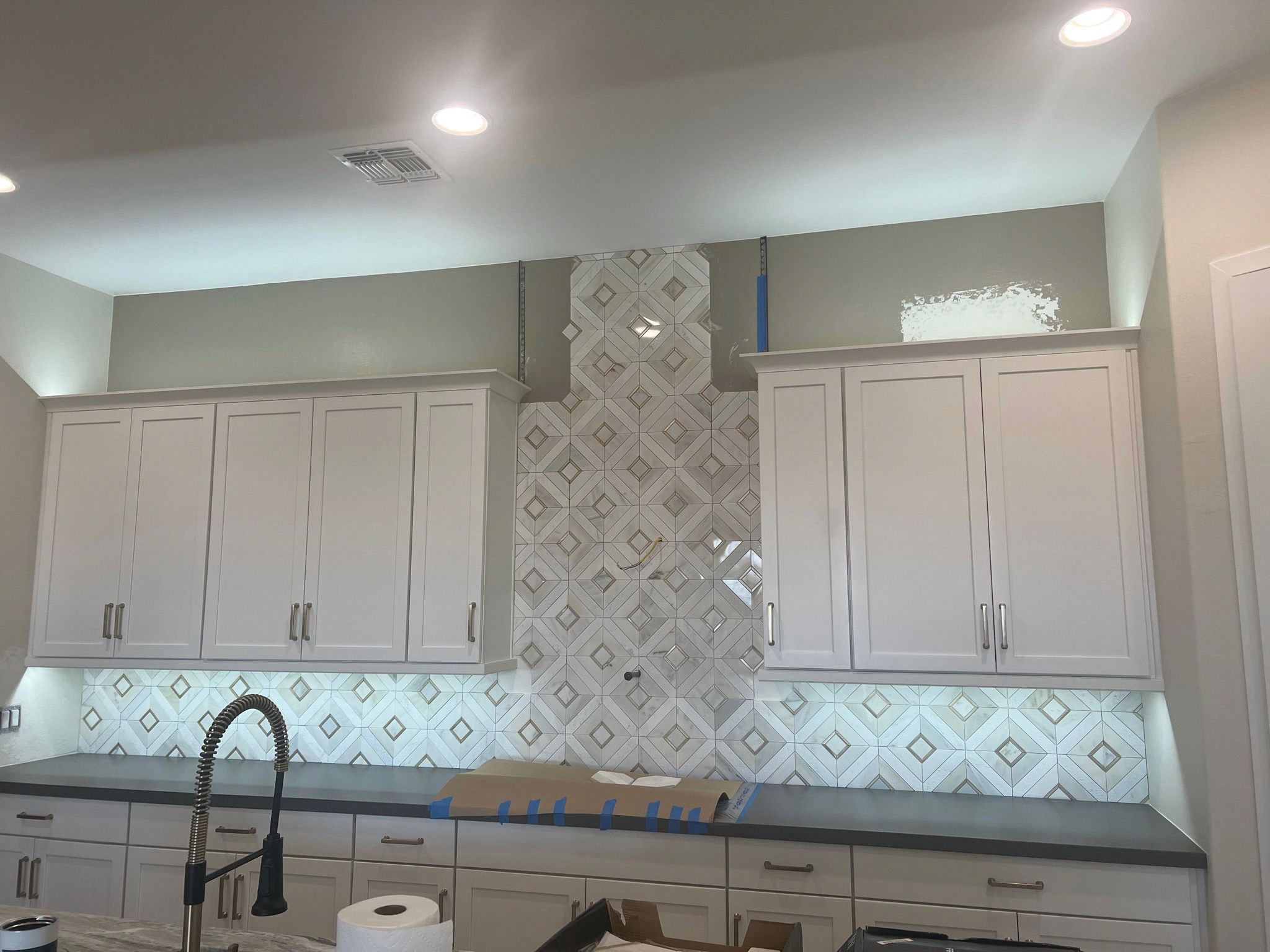 Elegant kitchen featuring white cabinets and a decorative geometric tile backsplash with under-cabinet lighting.