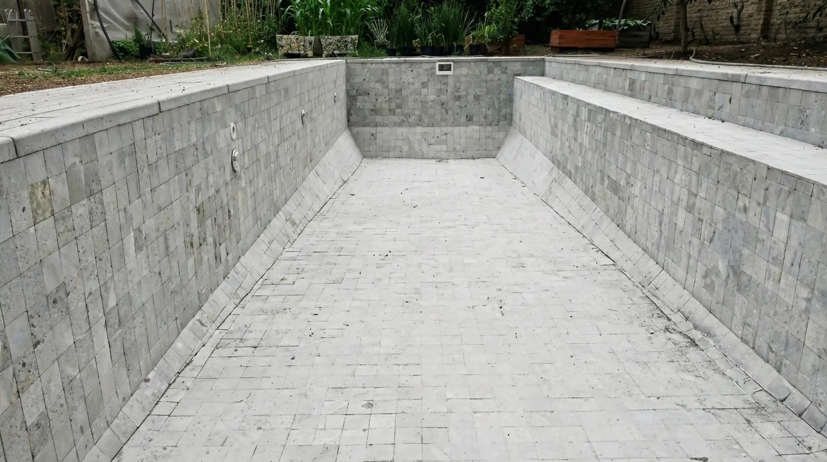 Obra finalizada de una gran pileta de hormigón armado vacía, destacando las amplias gradas laterales y el revestimiento completo en Piedra Bali seca.