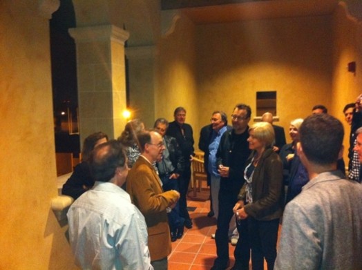A group of people sitting in an opened hallway and listening to a man giving a lecture.