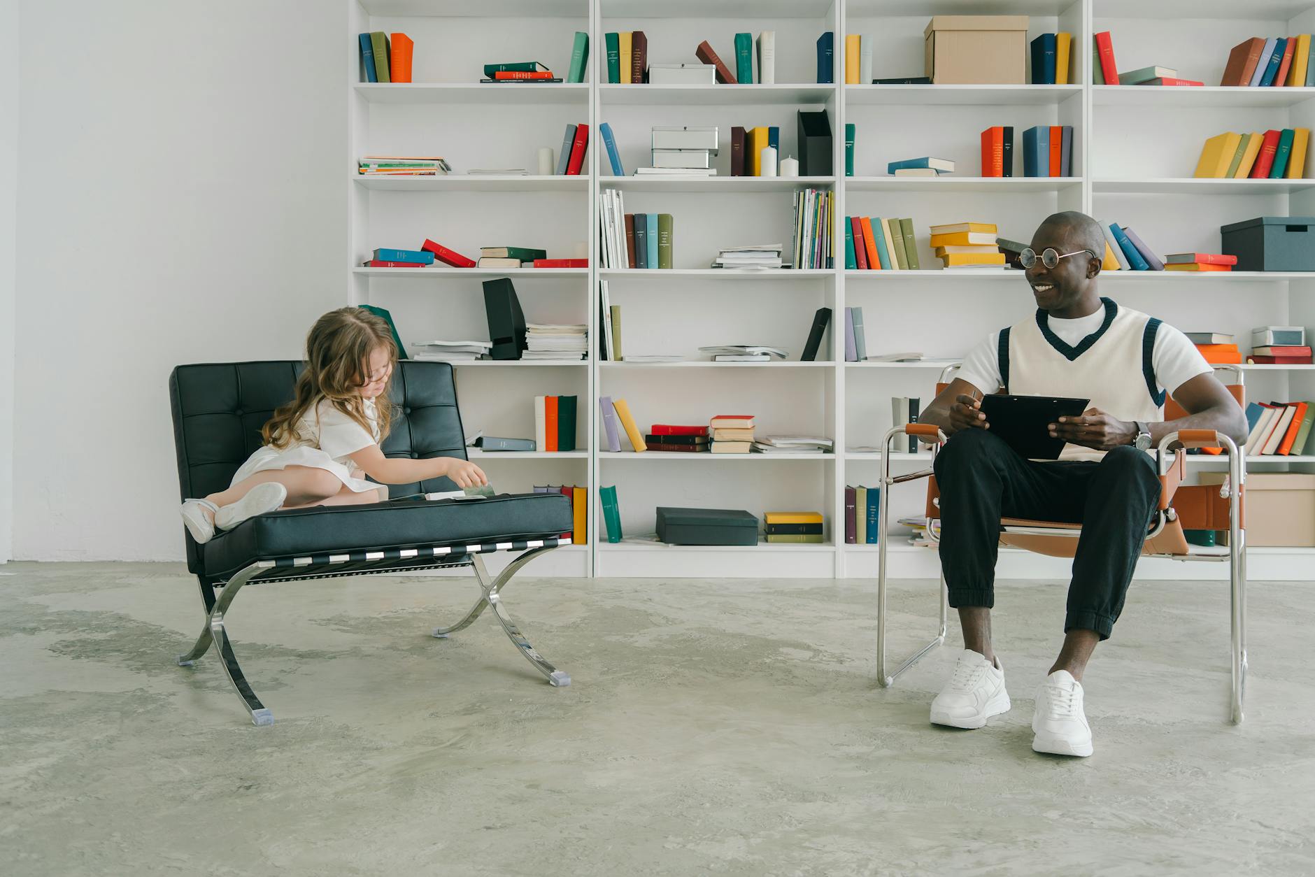 A young girl with headphones reads an e-book on a tablet while sitting in a cozy library beanbag chair.