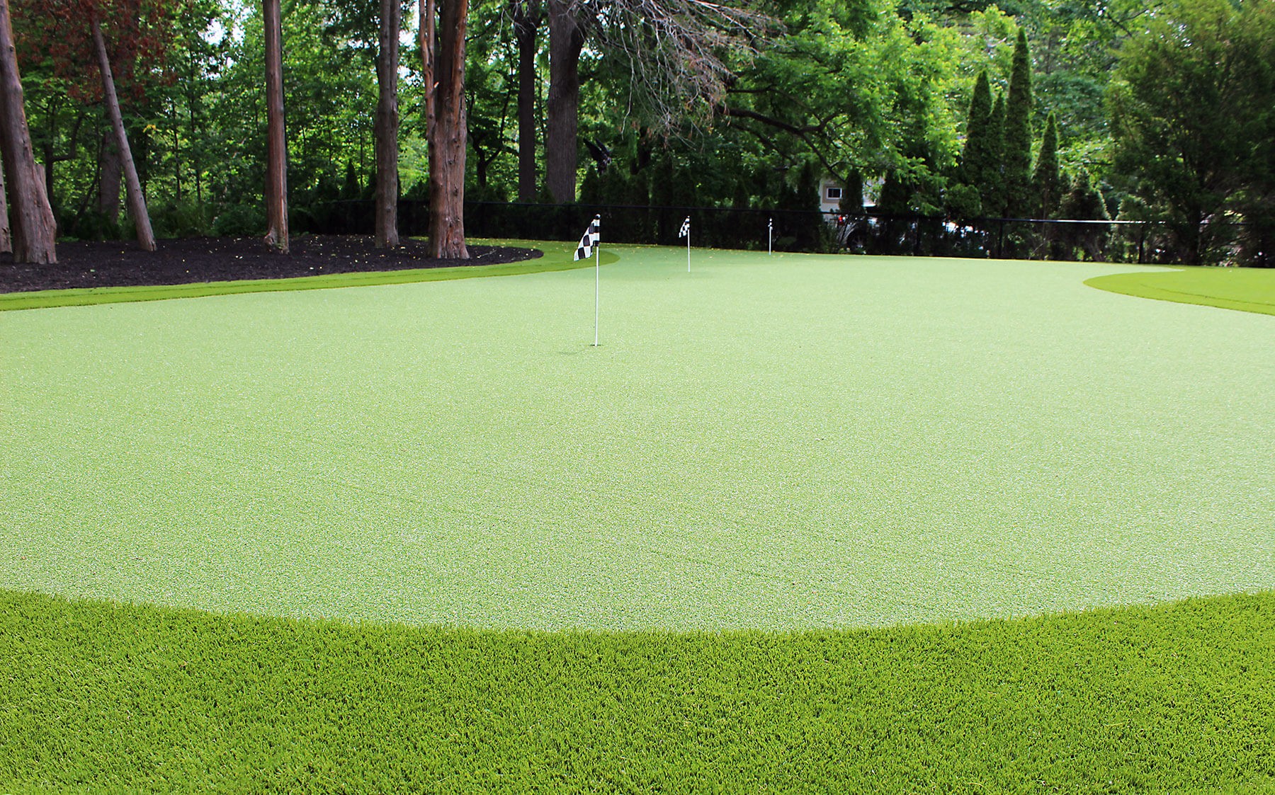 A serene backyard putting green surrounded by trees showcasing Golf Leisure artificial turf from AGL Grass North.