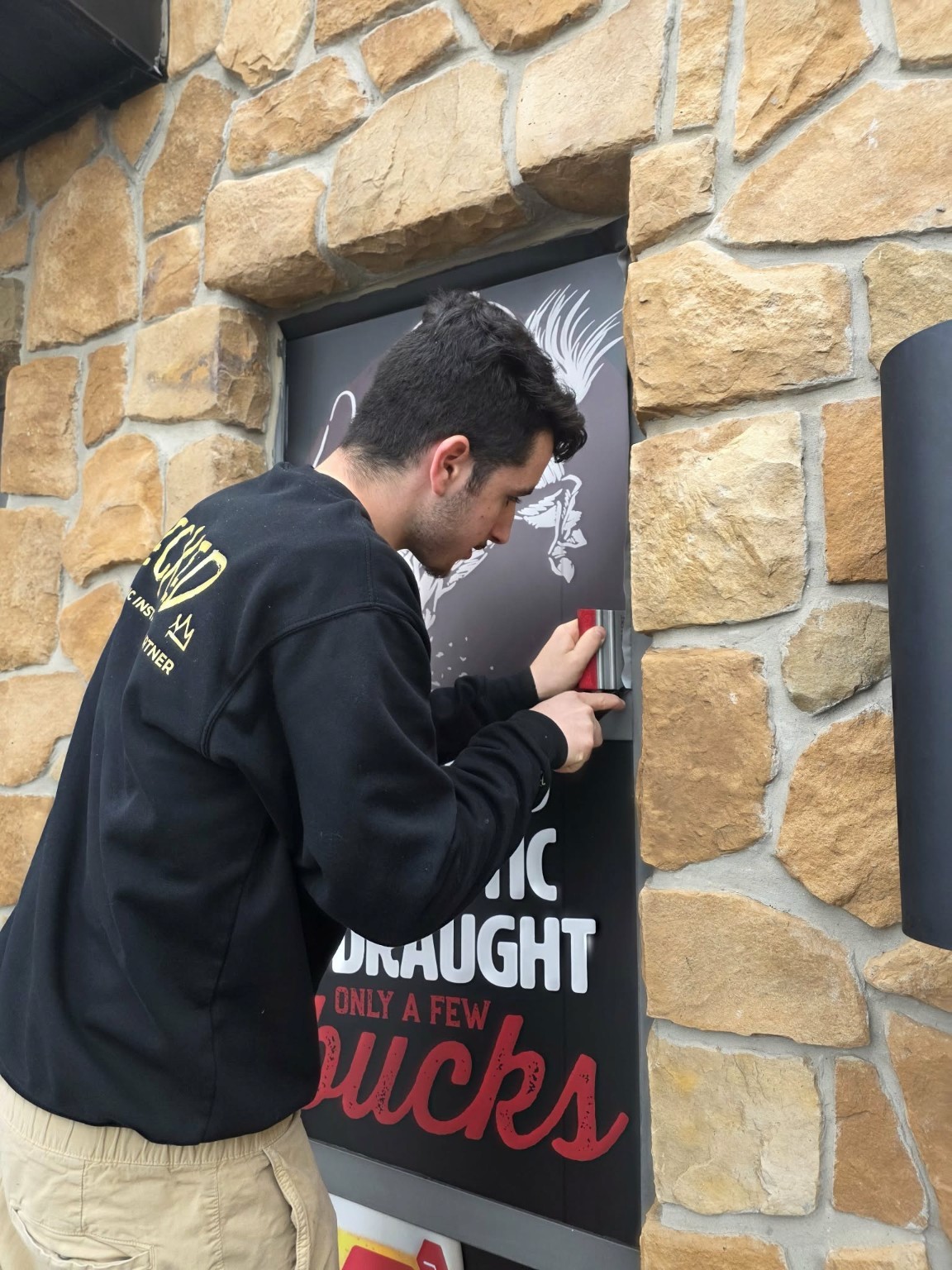 Close-up of a Wicked installer applying graphics to a stone-framed commercial window.