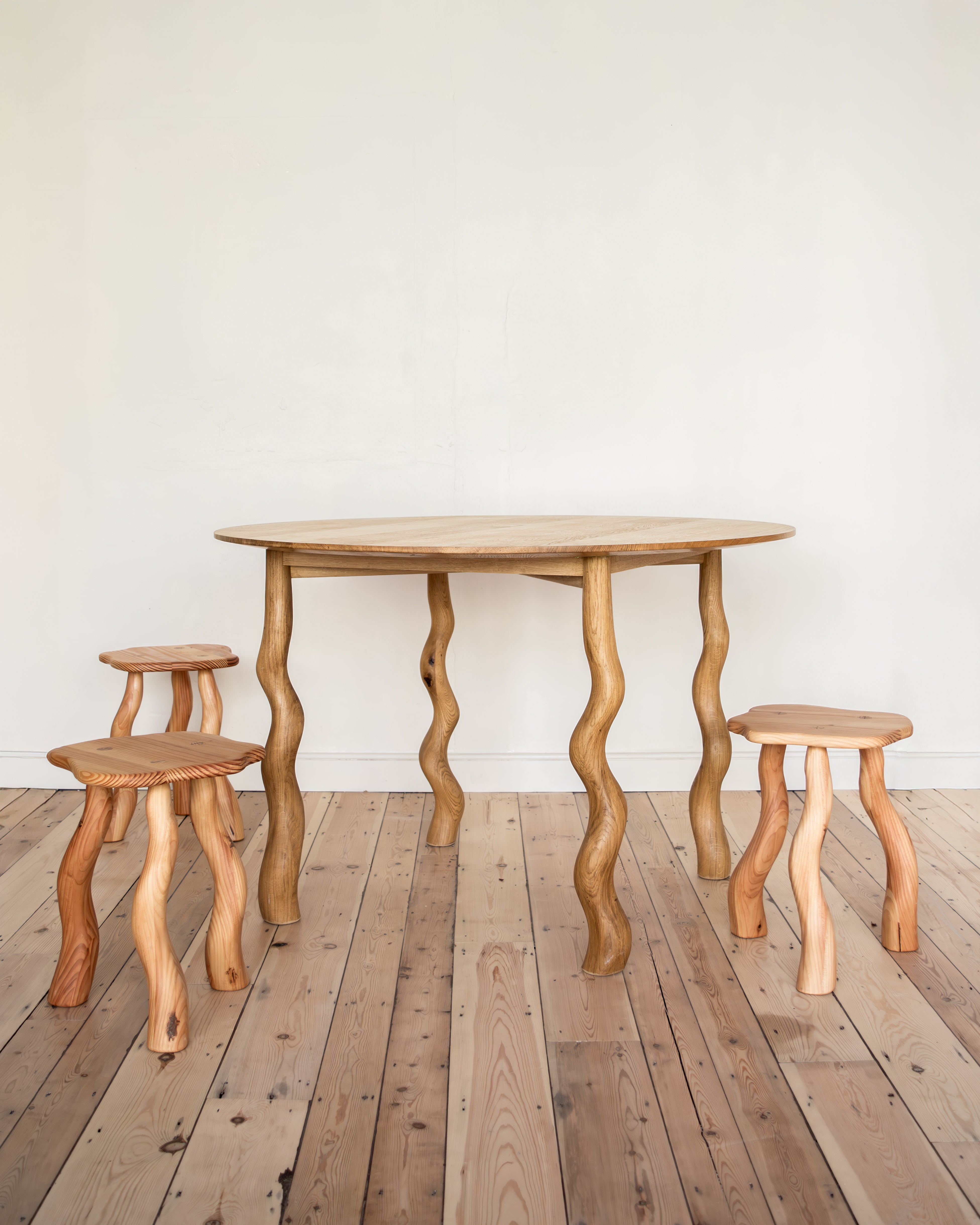 Wooden table and stools with wavy legs on a wooden floor against a white wall