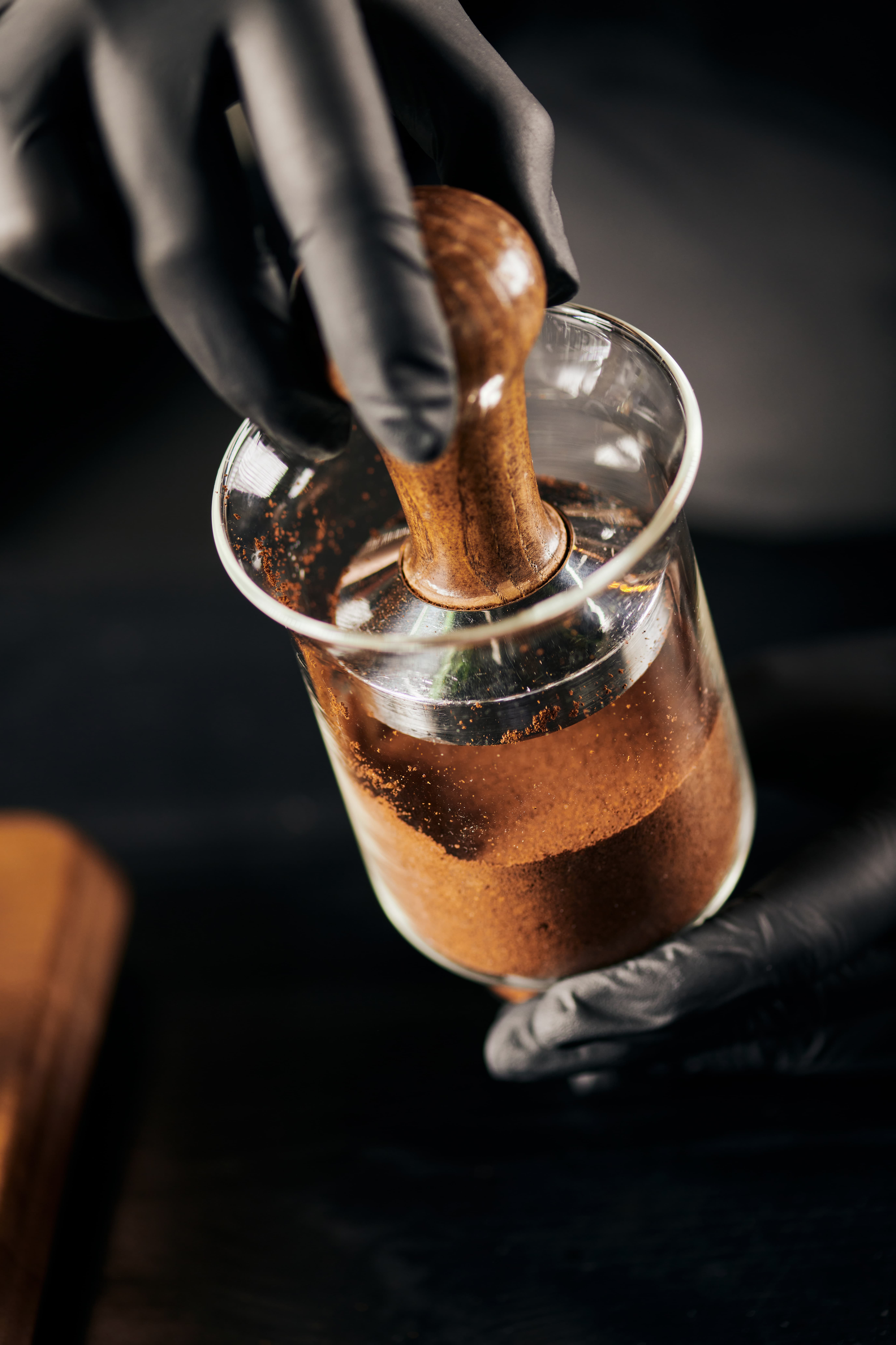 Close-up of a barista tamping coffee grounds in a portafilter, shot in a dark, moody style.