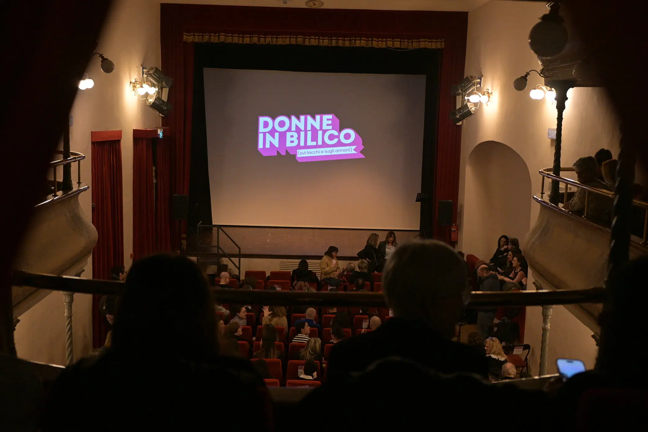 Sala del teatro verdi forlimpopoli, vista dal balconcino con pubblico seduto e schermo con proiezione logo donne in bilico