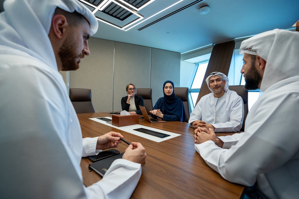 اجتماع عمل احترافي يضم خمسة أشخاص بملابس عربية تقليدية عصرية لمناقشة خطوات تاسيس شركة داخل مكتب حديث، يعكس التعاون والتركيز لرواد الأعمال في المنطقة العربية.