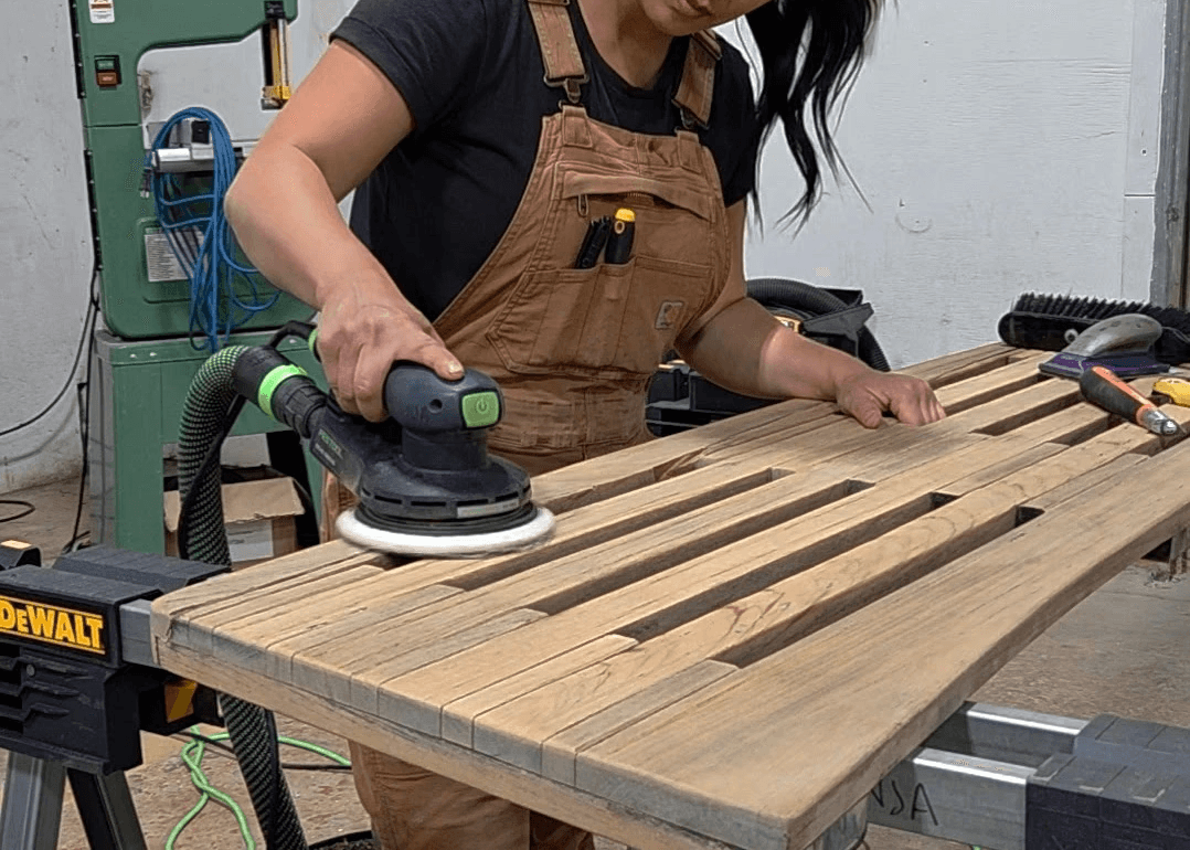 A woman sanding the teak platform of a boat to restore it