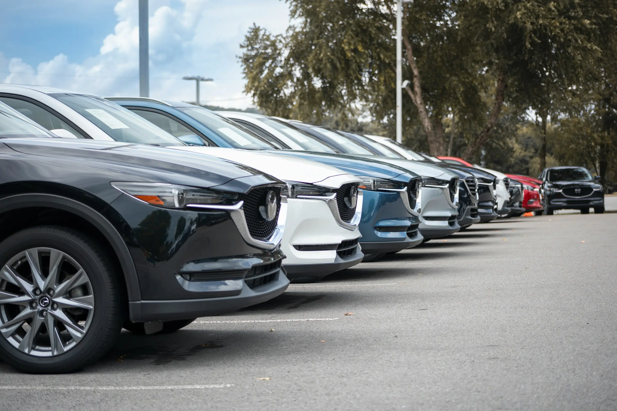 Row of new and pre-owned cars parked at a car dealership lot, showing organized vehicle inventory.