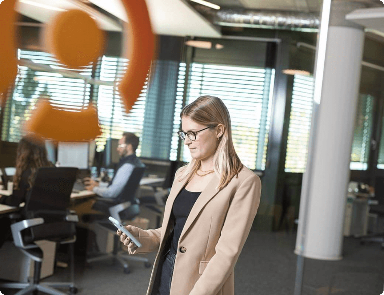 Female employee from the Sovendus Customer Service team walking through the office holding a smartphone