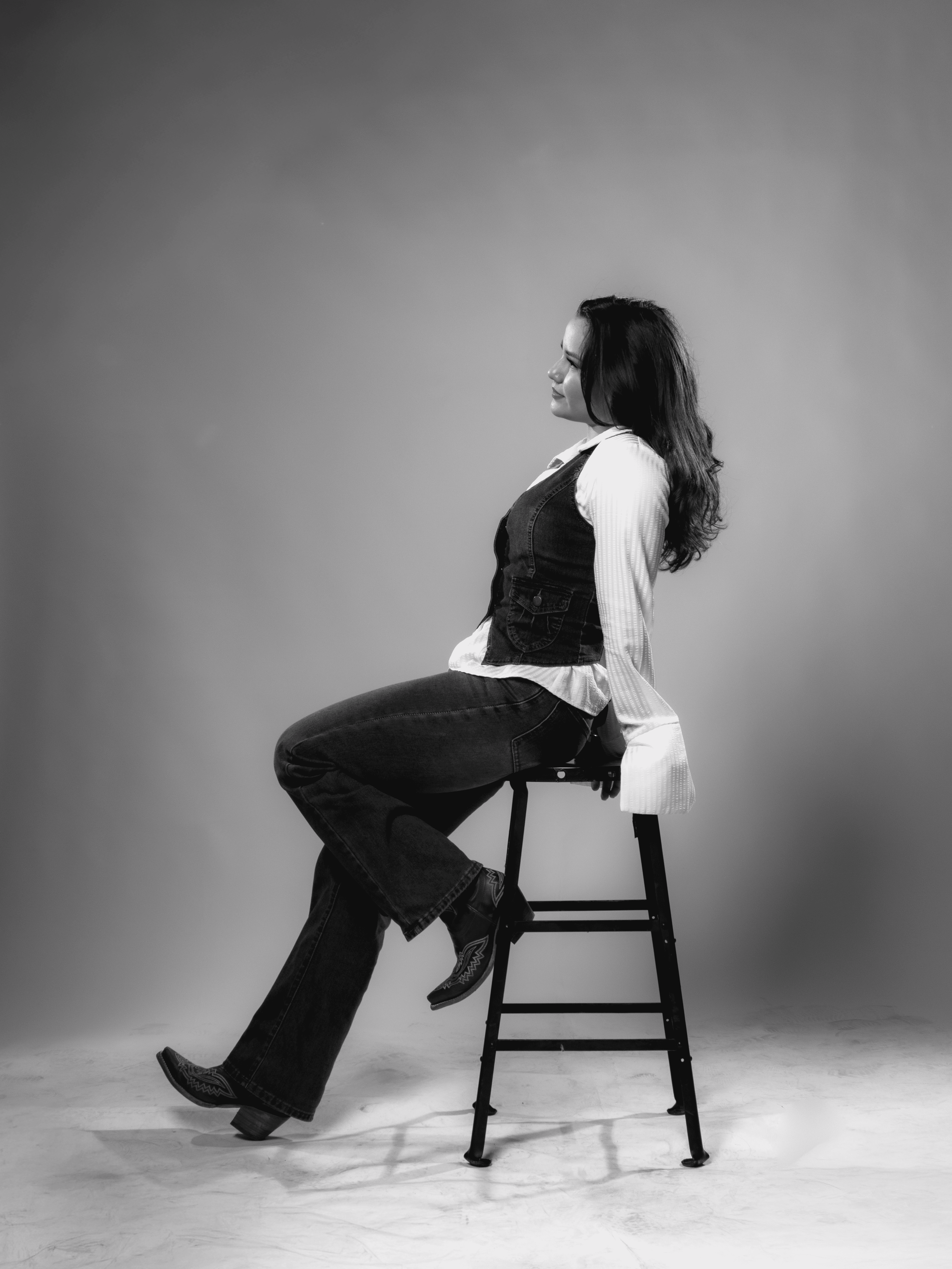 A thoughtful young person with dark hair gazes to the side, captured in soft black and white lighting.