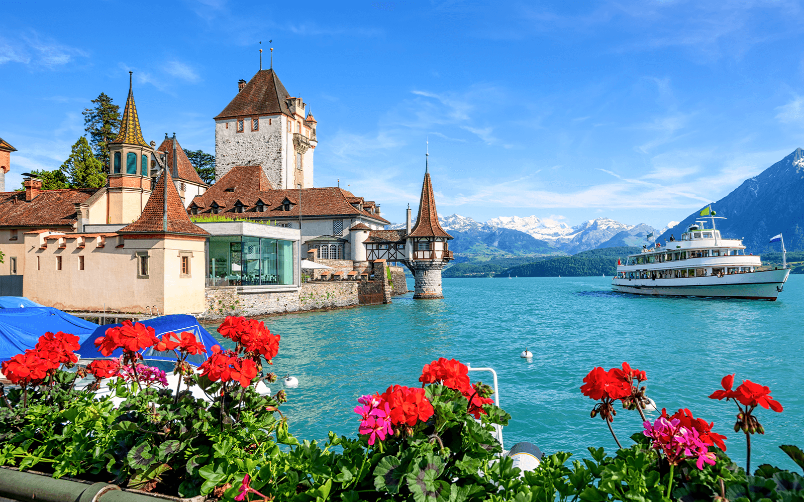 Oberhofen Castle on Lake Thun with a boat and Alps in the background, Switzerland.