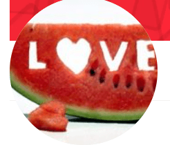 The image shows a slice of watermelon with the word "LOVE" carved into it, where the "O" is shaped like a heart. The bright red flesh of the watermelon contrasts with its green rind, giving it a playful and creative appearance.