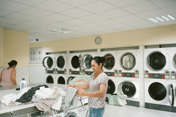 Woman folding clothes at a laundromat with large dryers in the background.