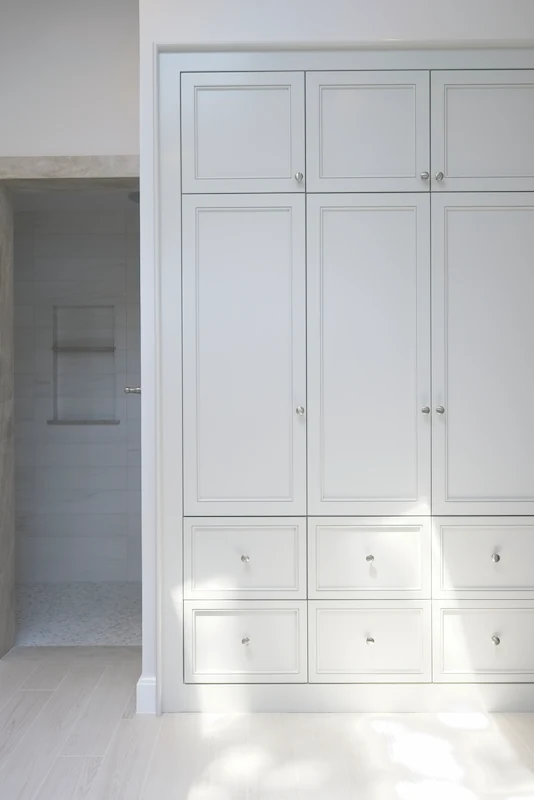 Tall primary bathroom storage cabinetry with subtle blue color seen next to the walk-in shower entrance from the Big Canyon Remodel project. Photo by Chris Darnall.
