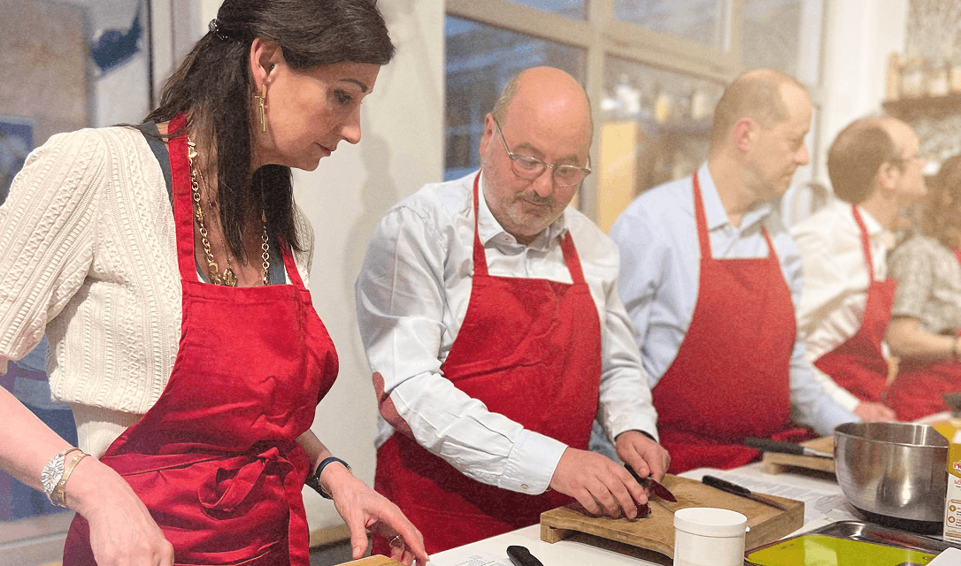 Personnes préparant des aliments en cuisine, portant des tabliers rouges, avec des ustensiles de cuisine sur le comptoir.