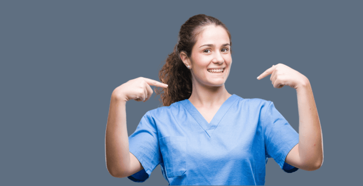 Smiling healthcare worker in scrubs pointing at herself on a gray background