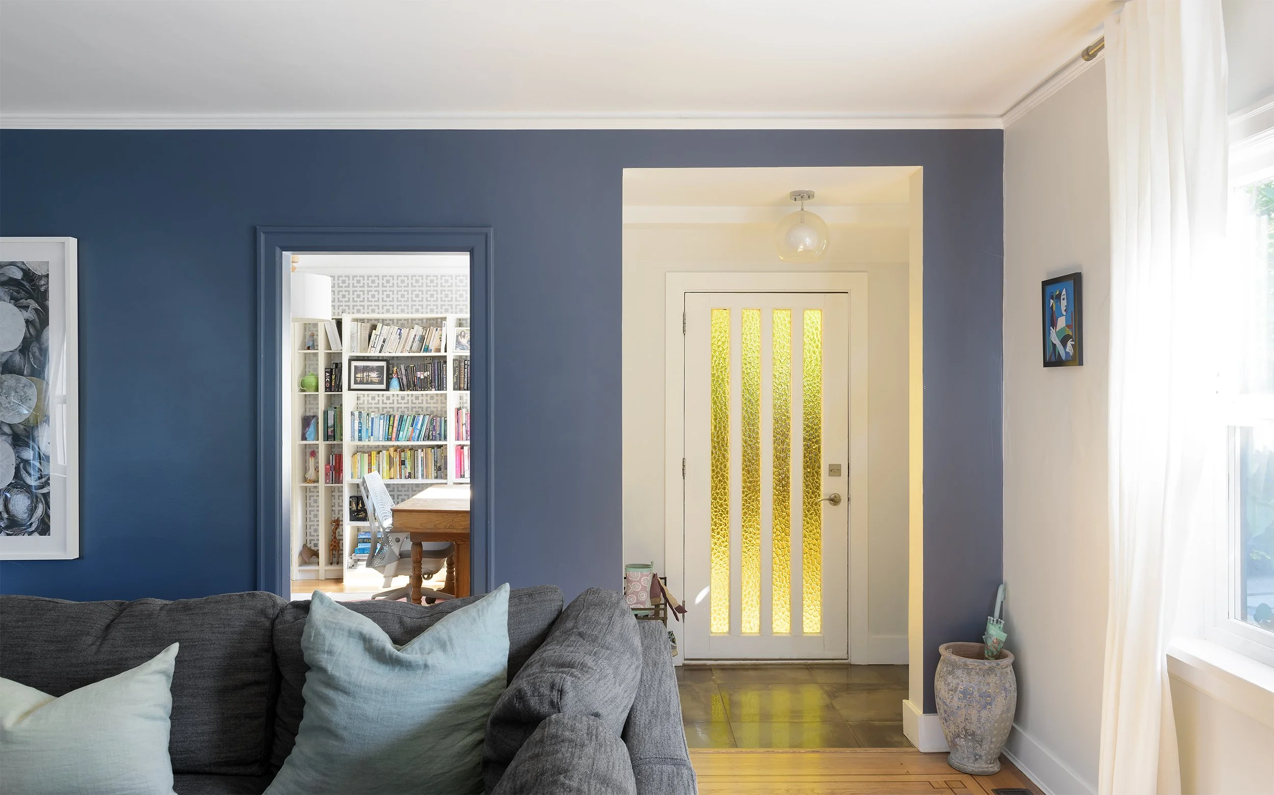 Modern two-story home with large glass windows, warmly lit interiors, and a balcony. Surrounded by trees and a manicured lawn at dusk. Cozy ambiance.