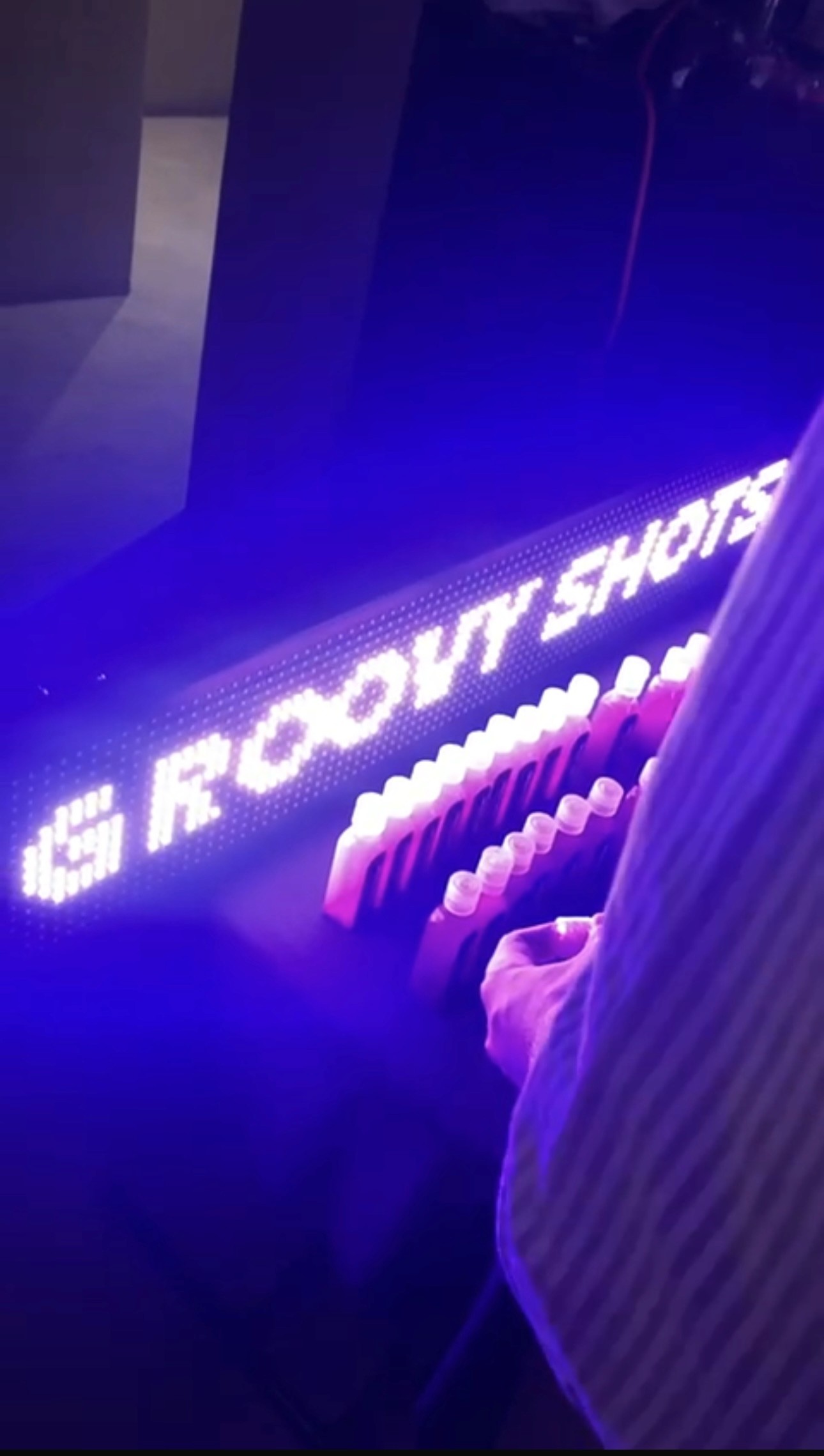 a row of shots in glass, with a background neon sign that says groovy shots