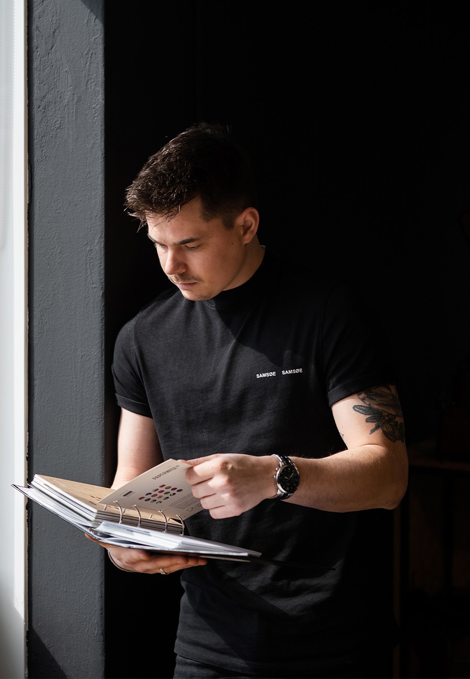 A person writing in a notebook at a sunlit table with a glass of water.