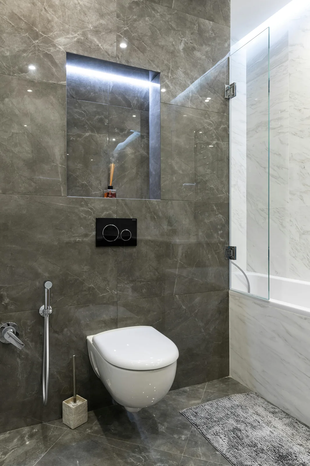 Modern bathroom with wall-mounted toilet, marble tiles, and glass partition