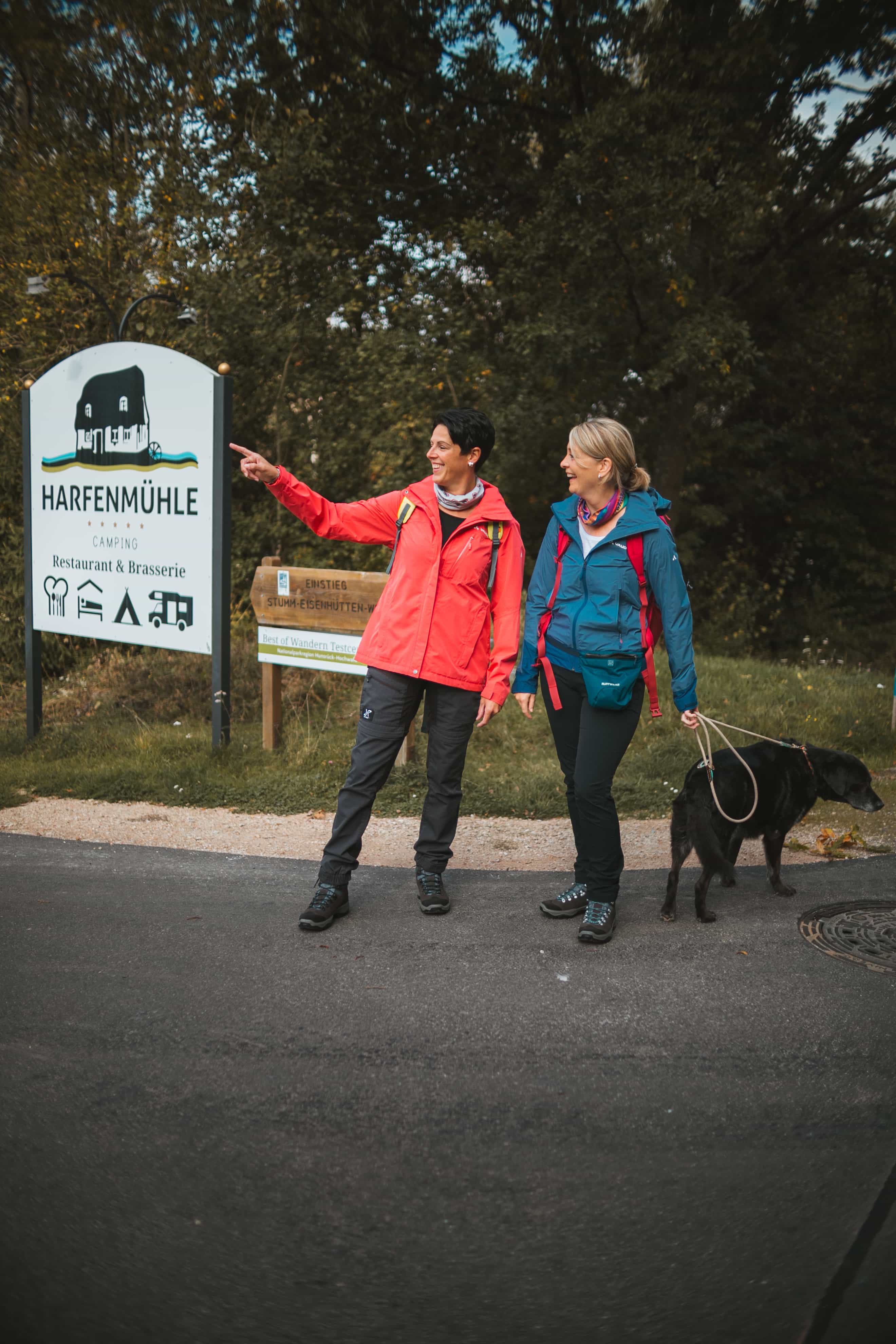 Zwei Wanderinnen sind am Einfahrtsschild vom Campingplatz Harfenmühle