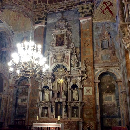Altare della chiesa decorato con statue intricate, murales e un lampadario ornato appeso al soffitto.