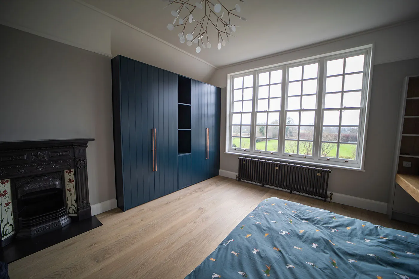 Modern bedroom with large blue wardrobe, a window with a view, and a patterned bedspread.