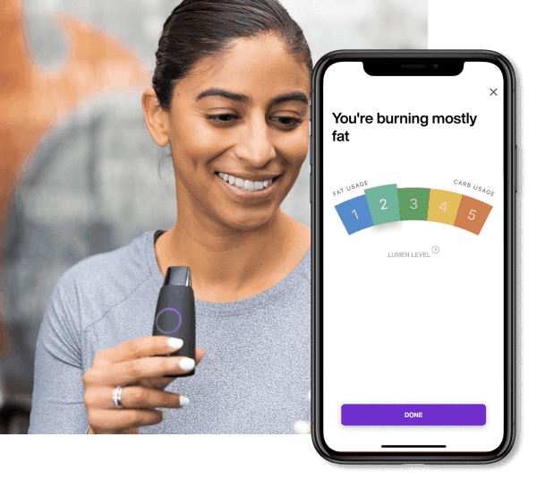 Smiling woman holding a Lumen metabolism tracker, with a phone displaying "You're burning mostly fat."