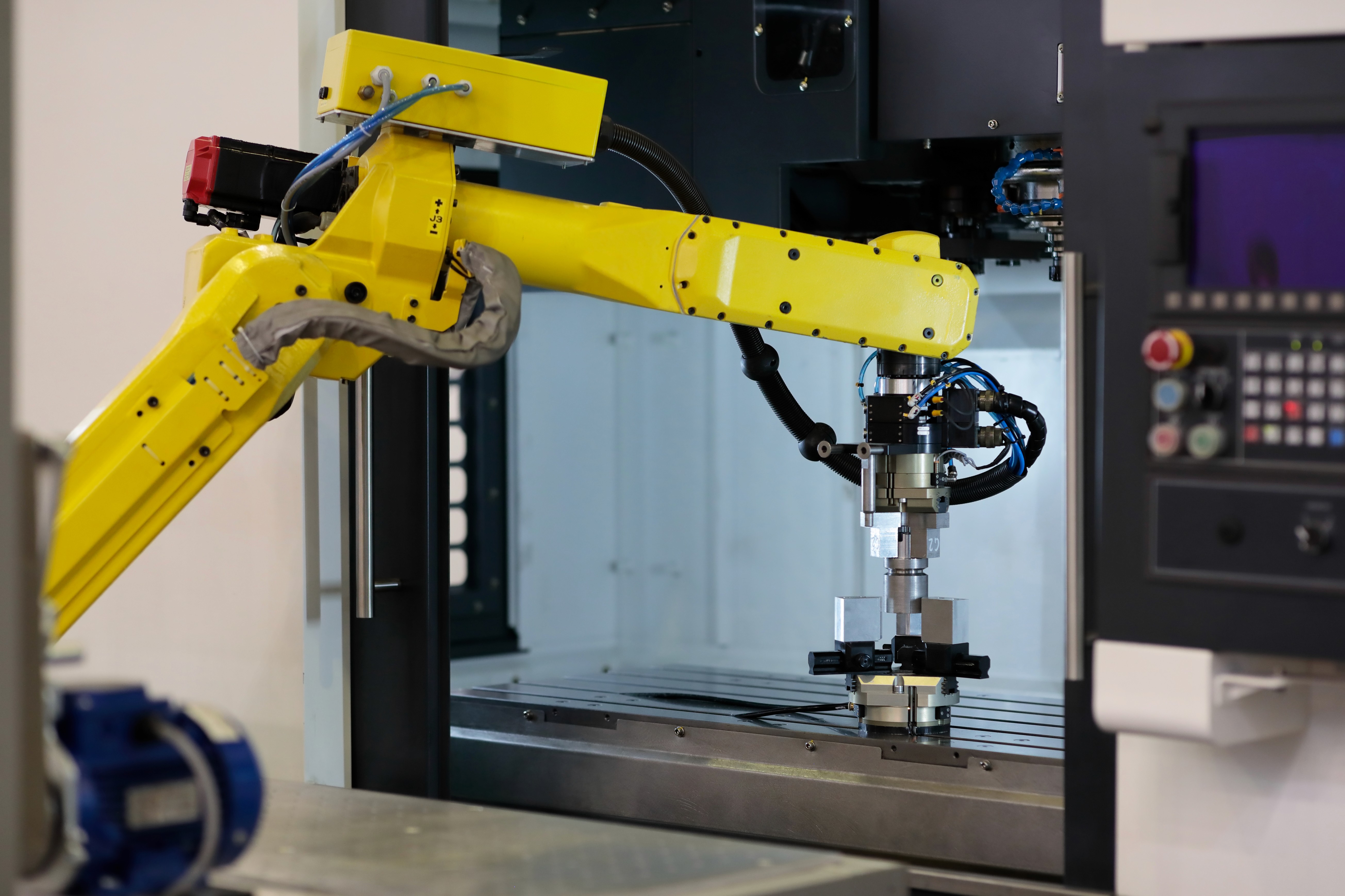 A yellow robotic arm is positioned near a machine, likely performing an automated task in a lab or workshop setting.