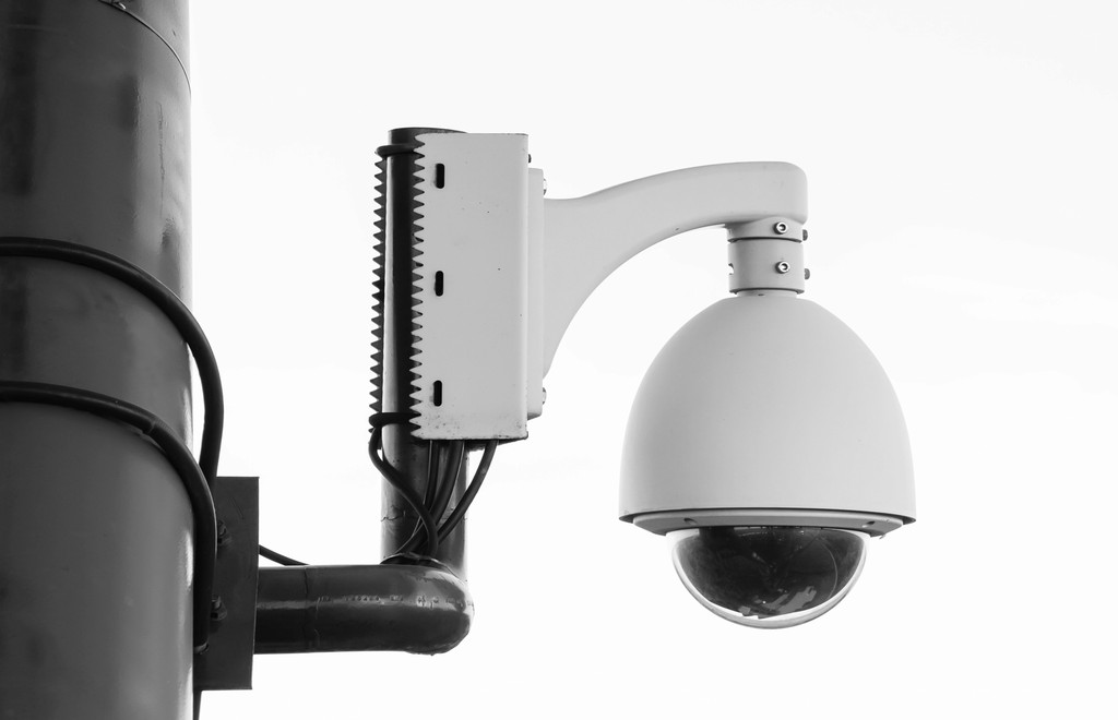 Dome security camera mounted on a pole with visible wiring and brackets.