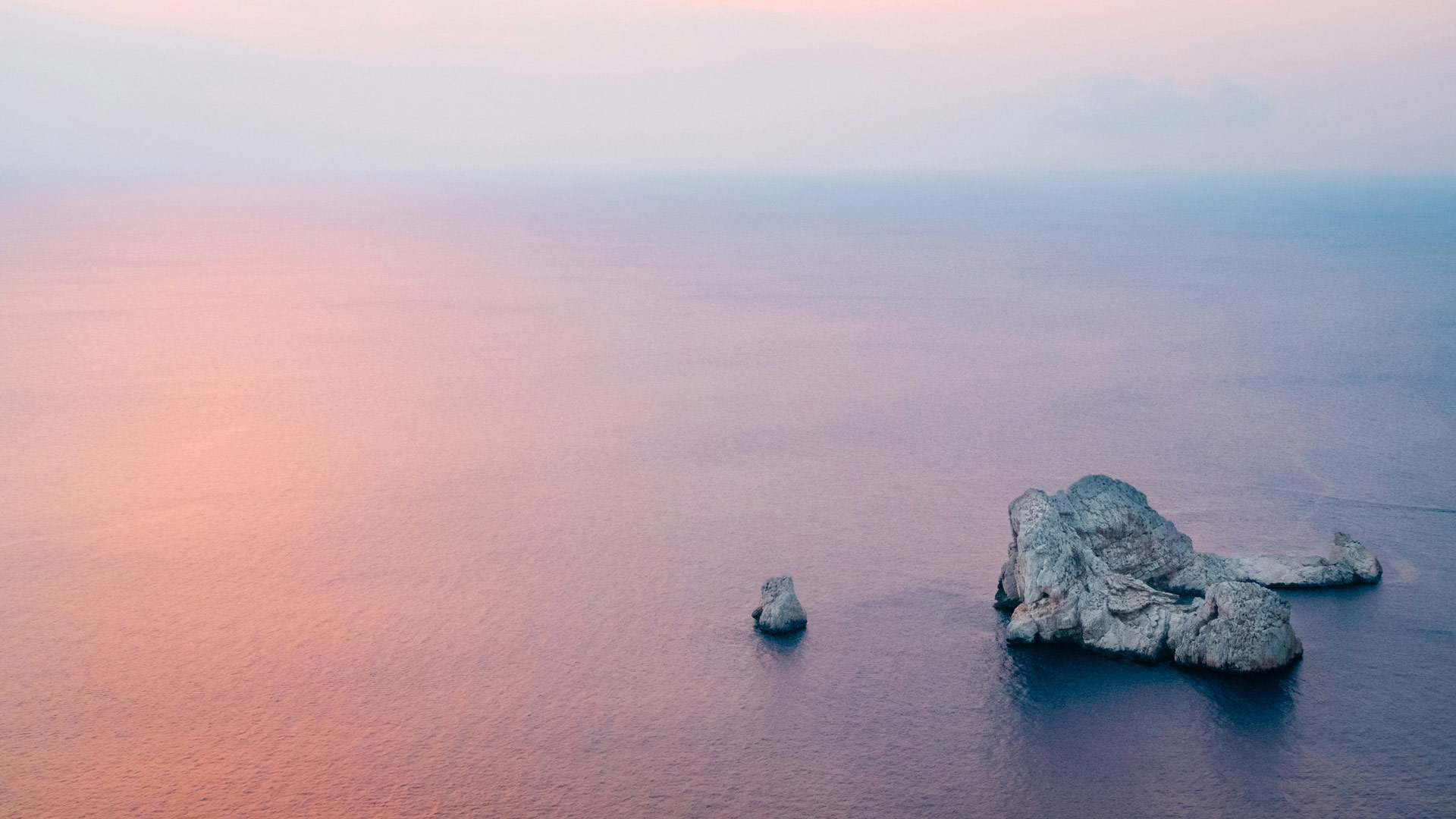 Aerial view of rocky islet in calm Mediterranean waters at sunset near Ibiza, symbolising privacy and seclusion.