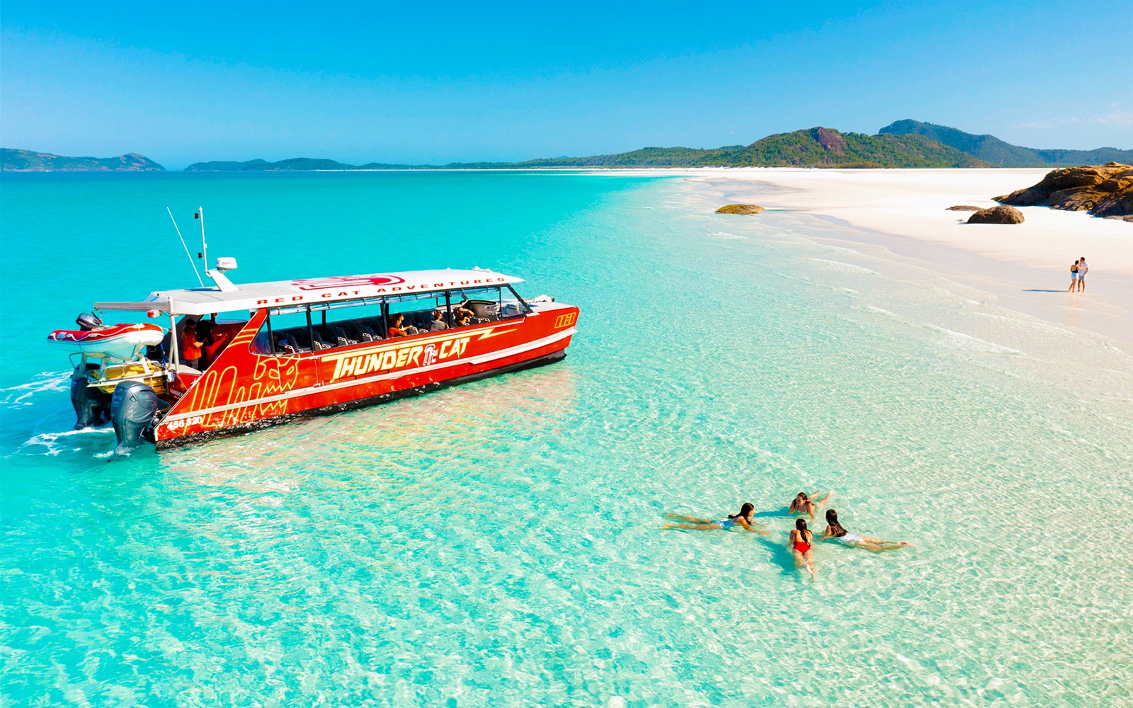 סירת טנדרקאט ליד חוף וויטסנדיי עם אנשים ששוחים במים צלולים.